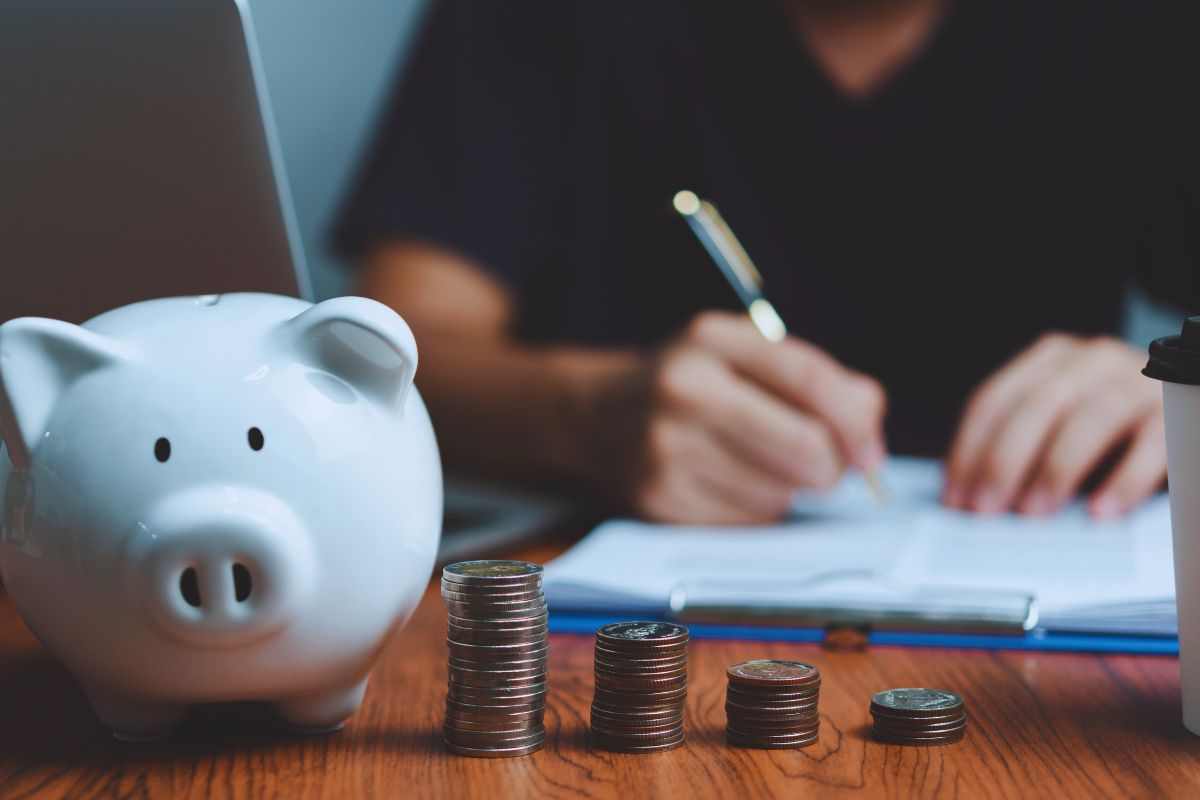 Persona che effettua dei conti, salvadanaio e pila di monete