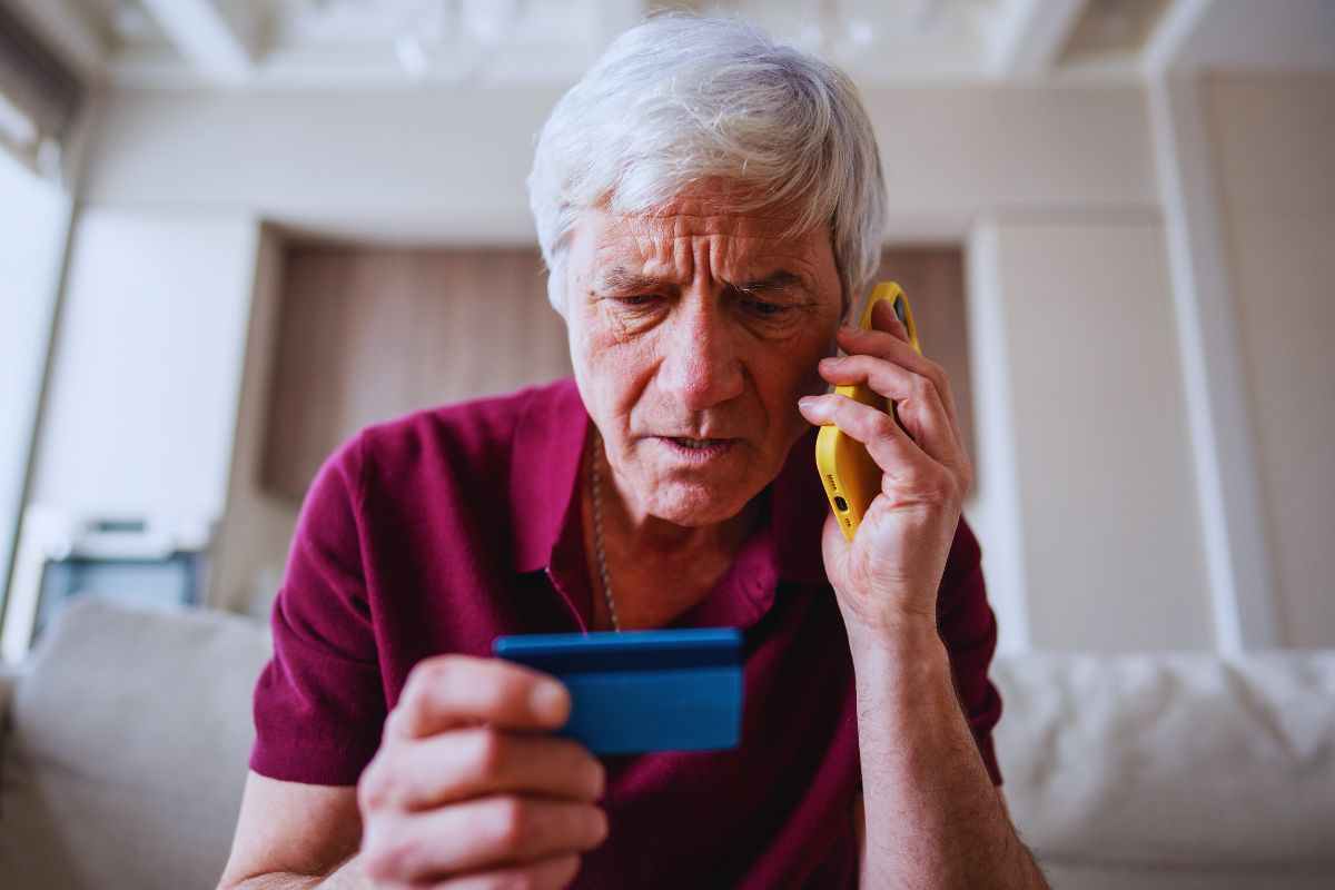 Uomo anziano al telefono che guarda carta di credito