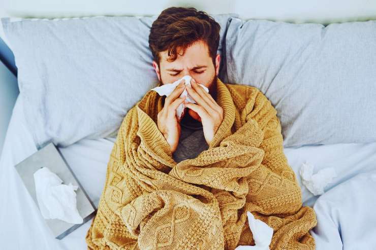 Uomo influenzato che si soffia il naso a letto