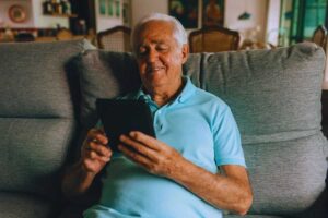 Anziano sorridente mentre usa tablet su divano