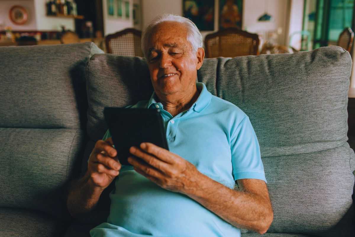 jene-stephaniuk-lkmGeyLItrw-unsplash-ls Anziano sorridente mentre usa tablet su divano